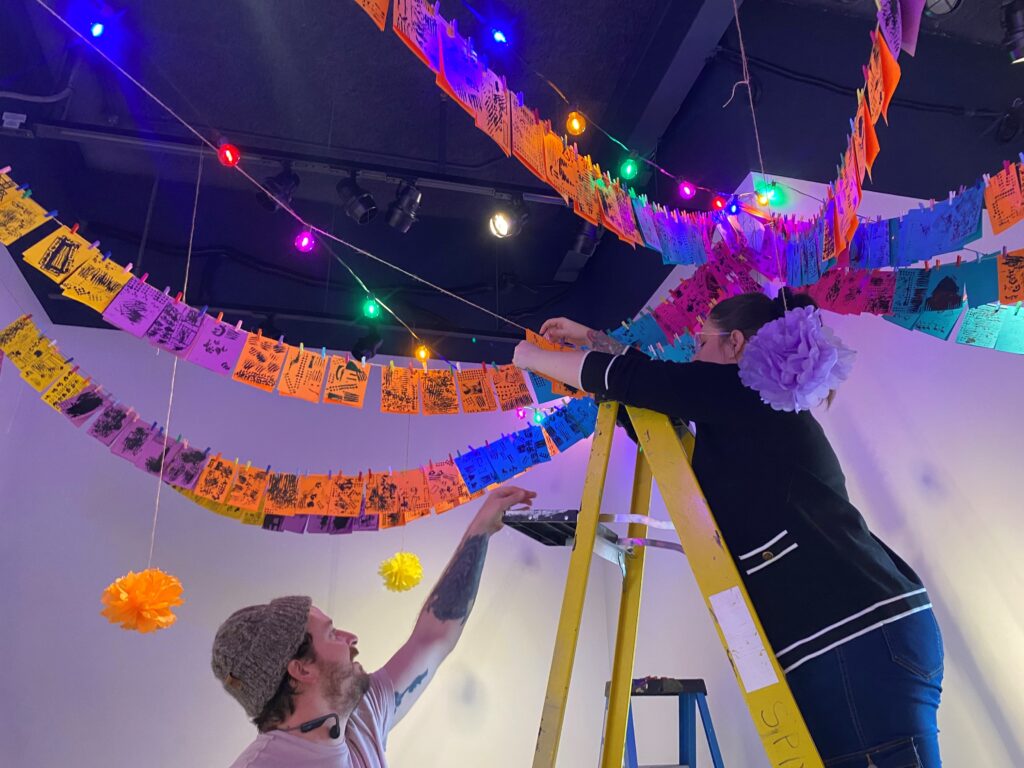 Volunteer helping staff hang 3rd grade projects.